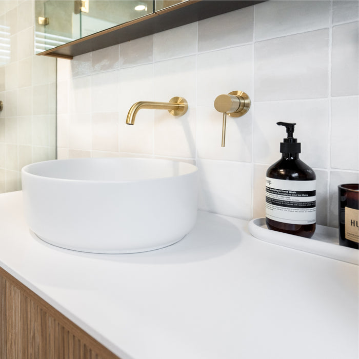Bathroom vanity with white sink, gold faucet, and a bottle of soap on a white countertop. Snow White Ella Zellige Tile 100 x 100 x 10mm Spanish Ceramic  | The Blue Space
